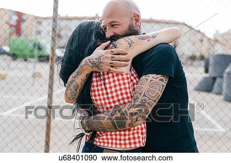 Mature tattooed hipster couple hugging by wire fence View Large Photo Image Stock Image - Mature tattooed hipster couple hugging by wire fence. Fotosearch