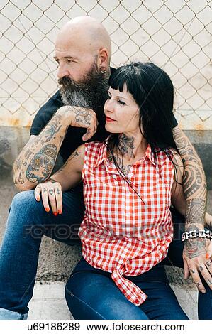 Mature tattooed hipster couple sitting on wall View Large Photo Image Stock Photo - Mature tattooed hipster couple sitting on wall. Fotosearch