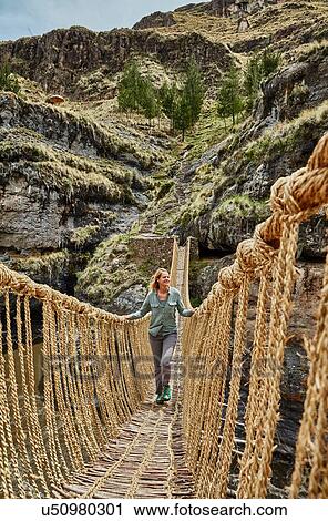 Stock Image - Mature woman crossing Inca rope bridge, Huinchiri, Cusco, Peru. Fotosearch
