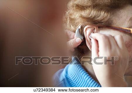 Mature woman helping senior woman insert hearing aid, close-up, differential focus View Large Photo Image Picture - Mature woman helping senior woman insert hearing aid, close-up, differential focus. Fotosearch