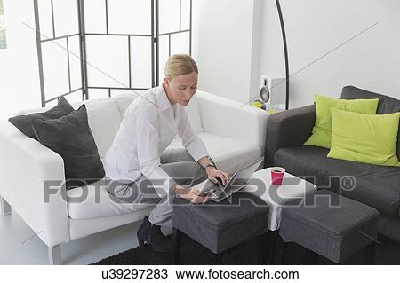 Mature woman sitting in modern living room and using laptop View Large Photo Image Stock Image - Mature woman sitting in modern living room and using laptop. Fotosearch