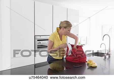 Stock Image - Mature woman unpacking groceries in modern kitchen. Fotosearch