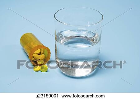 Stock Image - Medication and glass of water on a blue background.. Fotosearch