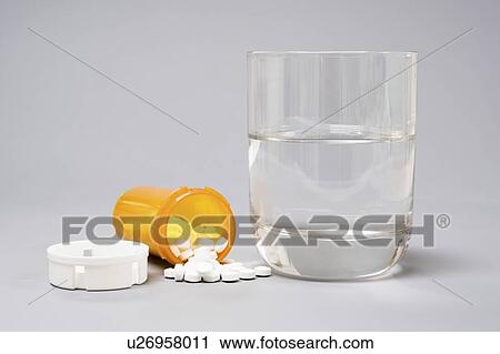 Stock Image - Medication and glass of water on a grey background.. Fotosearch