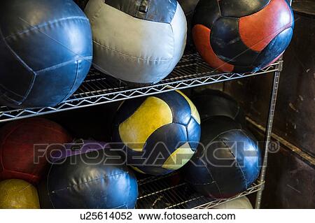 Stock Image - Medicine balls on metal shelf in gym, close-up. Fotosearch