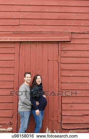 Stock Photograph - Mid adult couple standing in front of red barn. Fotosearch