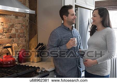 Stock Image - Mid adult couple standing in kitchen. Fotosearch