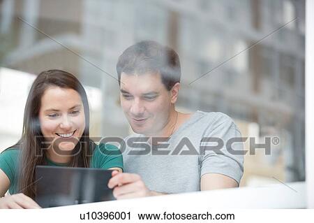 Mid adult man and woman in cafe, looking at digital tablet, view through window View Large Photo Image Stock Image - Mid adult man and woman in cafe, looking at digital tablet, view through window. Fotosearch