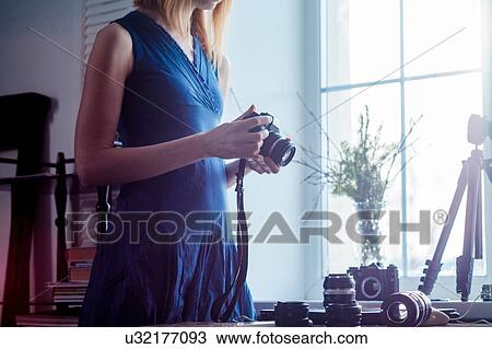 Mid adult woman, beside window, holding camera, camera lenses on table in front of her, mid section View Large Photo Image Stock Image - Mid adult woman, beside window, holding camera, camera lenses on table in front of her, mid section. Fotosearch