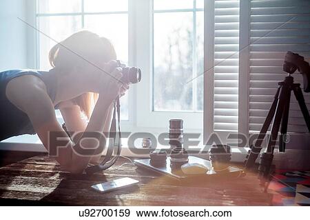 Mid adult woman, beside window, looking through camera, camera lenses on table in front of her View Large Photo Image Stock Photo - Mid adult woman, beside window, looking through camera, camera lenses on table in front of her. Fotosearch