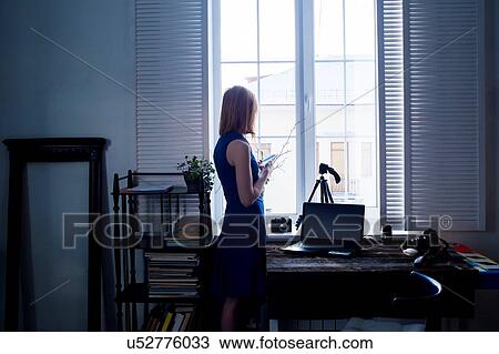 Mid adult woman, standing beside window, using smartphone, camera and laptop on table View Large Photo Image Stock Image - Mid adult woman, standing beside window, using smartphone, camera and laptop on table. Fotosearch