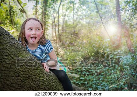 Stock Photo - Mischievous girl on tree trunk. Fotosearch