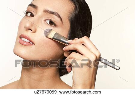 Stock Photo - MODEL RELEASED. Young woman applying foundation to cheek with make up brush.. Fotosearch