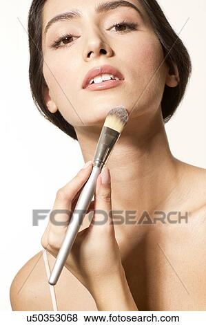 Stock Photo - MODEL RELEASED. Young woman applying foundation to chin with make up brush.. Fotosearch