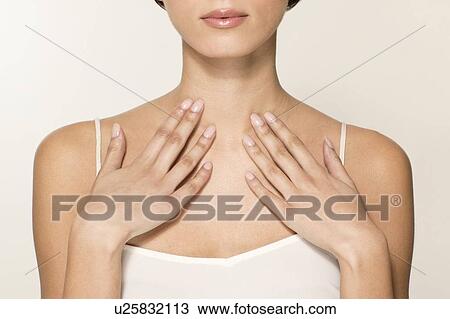 Stock Image - MODEL RELEASED. Young woman touching upper chest, cropped portrait.. Fotosearch