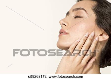 Stock Image - MODEL RELEASED. Young woman touching face with eyes closed, portrait.. Fotosearch