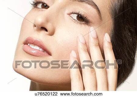 Stock Image - MODEL RELEASED. Young woman with fingers touching skin near eye, portrait.. Fotosearch