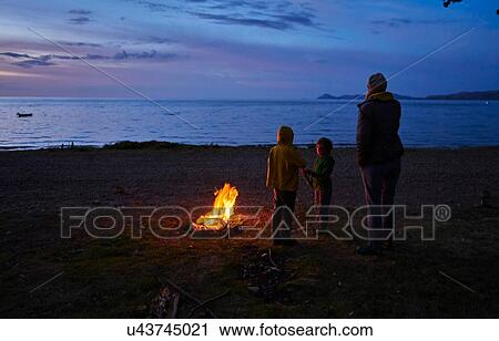 Stock Image - Mother and sons beside camp fire, looking at lake view, rear view, Copacabana, Oruro, Bolivia, South America. Fotosearch
