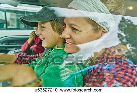Stock Image - Mother and sons inside vehicle, smiling, view through window. Fotosearch