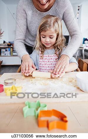 Stock Photograph - Mother helping daughter roll out cookie dough on kitchen table, mid section. Fotosearch