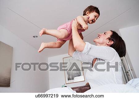 Stock Photo - Mother holding baby daughter in air, low angle view. Fotosearch