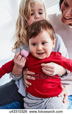Stock Photograph - Mother sitting with two young daughters, smiling. Fotosearch