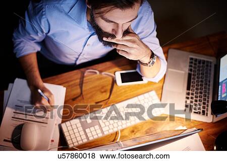 Overhead view of young businessman working at office desk at night View Large Photo Image Stock Photo - Overhead view of young businessman working at office desk at night. Fotosearch