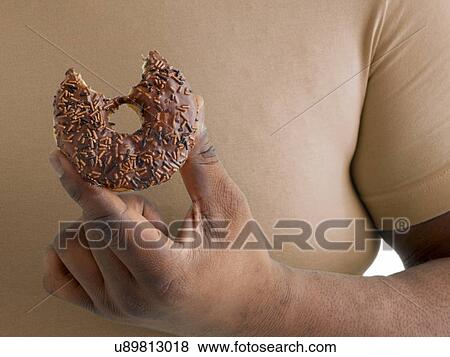 Stock Photo - Overweight man holding a doughnut with a missing bite.. Fotosearch