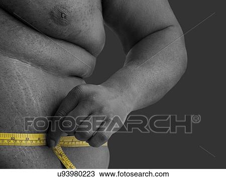 Stock Image - Overweight man measuring his waist with a tape measure.. Fotosearch