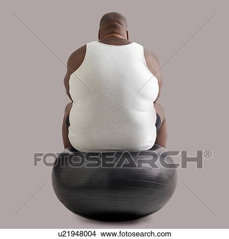 Picture - Overweight man sitting on an exercise ball, rear view.. Fotosearch