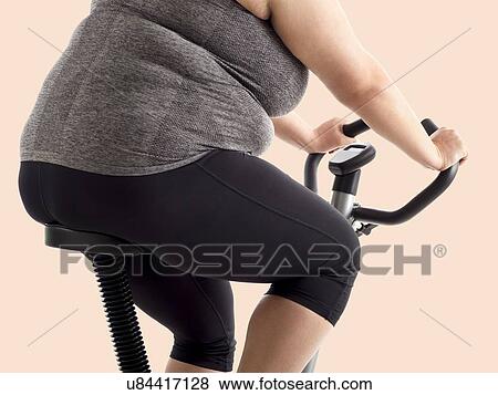 Stock Photo - Overweight woman on exercise bike.. Fotosearch