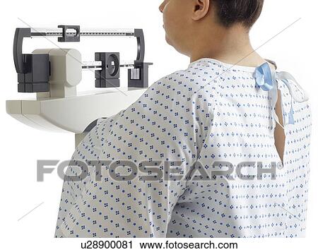 Stock Image - Overweight woman using hospital weighing scales.. Fotosearch