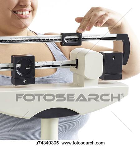 Stock Photography - Overweight woman using weighing scales, smiling.. Fotosearch