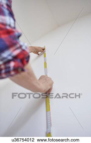 Stock Image - Person measuring white wall. Fotosearch