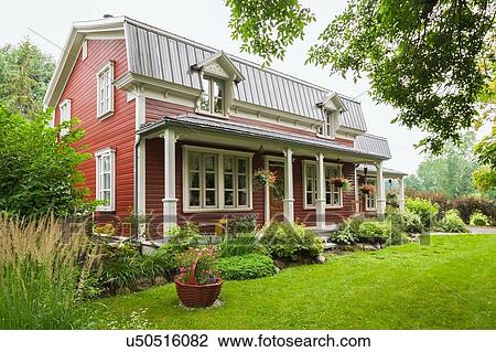 Stock Image - Pinewood plank house facade with mansard roof and landscaped garden, Quebec, Canada. Fotosearch