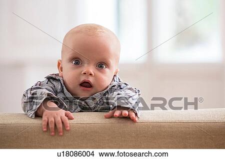 Picture - Portrait of baby boy, climbing on sofa. Fotosearch