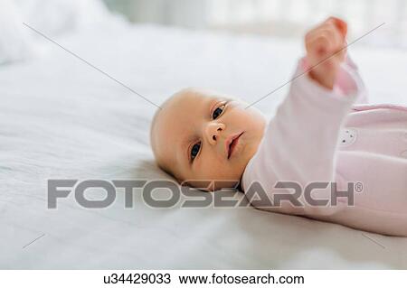 Stock Image - Portrait of baby girl lying on bed. Fotosearch