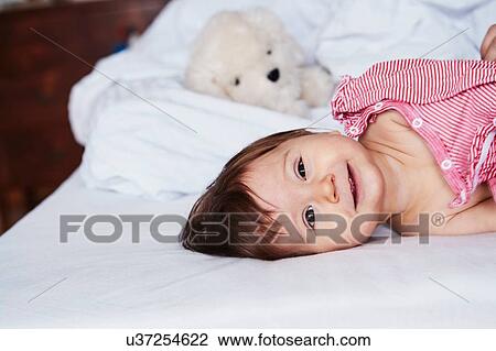 Stock Image - Portrait of baby girl lying on bed, smiling. Fotosearch