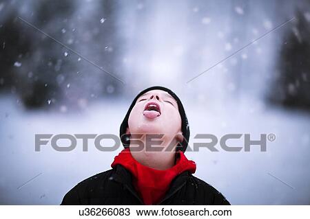 Stock Image - Portrait of boy catching falling snow on tongue. Fotosearch