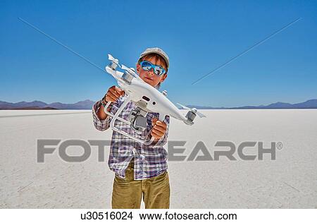 Picture - Portrait of boy on salt flats, holding drone, Salar de Uyuni, Uyuni, Oruro, Bolivia, South America. Fotosearch
