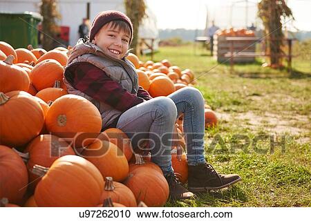 Stock Image - Portrait of boy sitting on stack of harvested pumpkins. Fotosearch