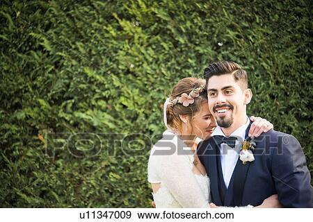 Stock Photo - Portrait of bride and bridegroom, hedge in background. Fotosearch