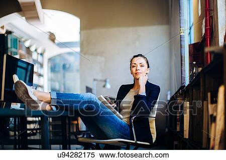 Stock Photography - Portrait of businesswoman sitting at desk, feet up on desk. Fotosearch