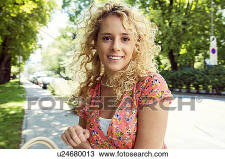 Stock Image - Portrait of curly haired blonde woman looking at camera smiling. Fotosearch