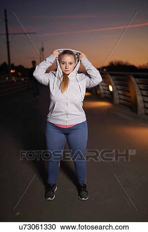 Portrait of curvaceous young woman training, getting hoody ready on footbridge at night View Large Photo Image Stock Image - Portrait of curvaceous young woman training, getting hoody ready on footbridge at night. Fotosearch