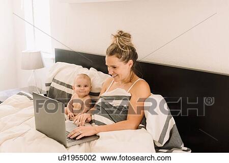 Portrait of cute baby girl sitting up in bed while mother using laptop View Large Photo Image Stock Image - Portrait of cute baby girl sitting up in bed while mother using laptop. Fotosearch