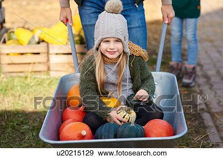 Stock Photo - Portrait of girl in wheelbarrow with pumpkins at pumpkin patch. Fotosearch