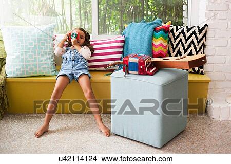 Portrait of girl leaning on window seat photographing with toy camera View Large Photo Image Picture - Portrait of girl leaning on window seat photographing with toy camera. Fotosearch