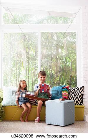 Stock Photo - Portrait of girl on window seat with boy practicing accordion. Fotosearch