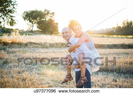 Stock Photograph - Portrait of heterosexual couple in field, man carrying woman on back. Fotosearch